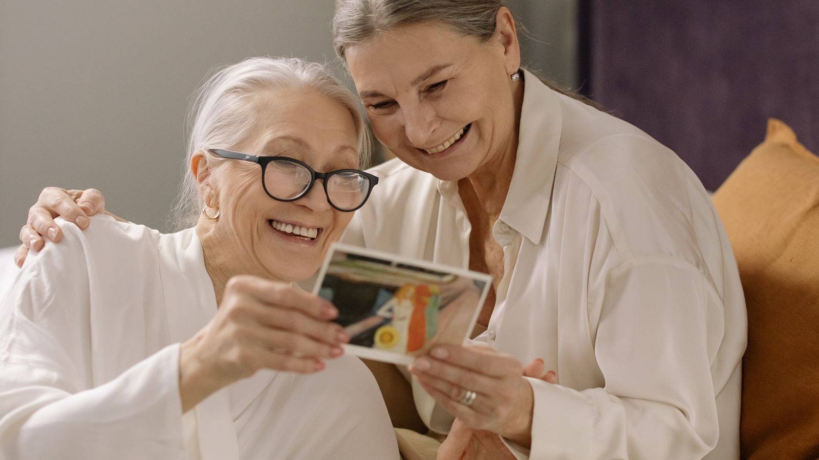 An older woman and a younger companion look through a photo album together, talking about the pictures